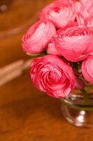 Glass vase of pink ranunculus on wooden surface