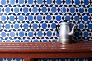 Old metal coffee pot on wooden table against tiled wall