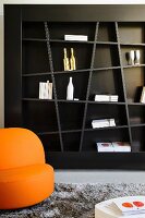 Abstract shelving on dark brown wall and orange armchair in living room