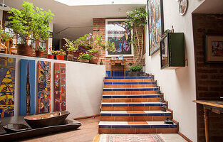 Geflieste Treppe im offenem Wohnbereich mit vielen Zimmerpflanzen und Gemälden an der Wand