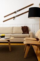 Wohnzimmer im skandinavischen Stil mit beigefarbener Couch und Holzstühlen; über der Couch antike Skier