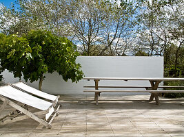 Deckchairs, table and benches on terrace in green surroundings