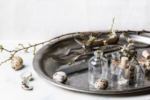 Quail eggs, vintage tableware and vials with blossom branches on old metal tray