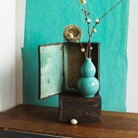 Bird's nest on wooden cabinet behind turquoise vase of flowering twigs
