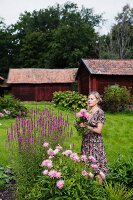 Woman cutting flowers in garden with simple wooden buildings in background
