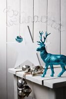 White wooden table with white wooden star, turquoise glittery reindeer, silver baubles and Christmas motto formed from wire in background