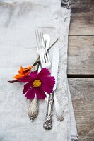 Silberbesteck mit Blumen und Leinenserviette auf Holztisch
