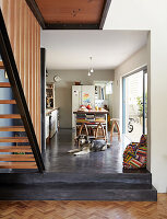 Kitchen with black concrete floor, dog in front of kitchen island and vintage bar stool, stairs in the foreground