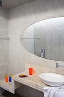 Washstand with white china basin on stepped concrete surface and oval mirror on concrete wall