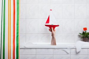 A hand sticking out of a bathtub holding a toy boat