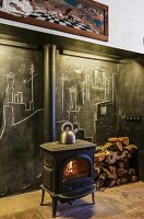 Wood-burning stove in front of blackboard wall with chalk drawings and stacked firewood in rustic ambiance