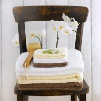 Towels, soap and bath brush in front of orchid on wooden chair