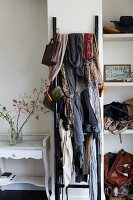 Numerous scarves hung on wooden ladder flanked by vintage table and bags on shelving