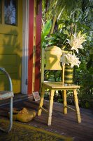 Holzschuhe & gelber Stuhl mit weißem Lilienstrauss auf Veranda