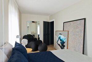 Double bed in modern bedroom with sculptural armchair by Gaetano Pesce and large, modern artworks leaning against wall