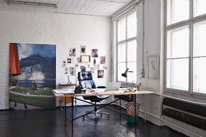Eiermann table and executive chair in loft apartment; landscape photo and mood board in background