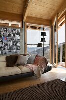 Leather sofa below collection of photos on wall next to group of standard lamps in front of panoramic window in wood-clad chalet interior