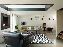 Black leather armchair and sofa around coffee table on black and white patterned rug in living room with skylight