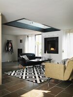 Black leather armchair and sofa around coffee table on black and white patterned rug in living room with skylight