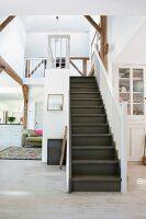 Dunkle Holztreppe mit weißem Geländer in offenem Wohnraum, seitlich Blick in Küche