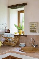 Übereck-Küchenzeile mit beigefarbenen Wandfliesen und gefliester Arbeitsfläche, Geschirrabtropfregal vor Fenster