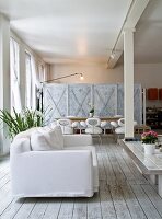 White sofa on simple wooden floor in front of dining area against partition