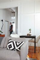 Cushion with graphic pattern on grey sofa in front of small dining table and retro chairs