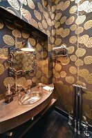 Curved washstand with silver sink, wallpaper with pattern of gold leaves and mirror with vintage frame in bathroom