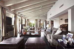 Leather ottomans and sofa set in open-plan interior with white-painted wood-beamed ceiling