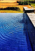 Infinity pool with half-height wall and integrated water spout; view of Mediterranean landscape in background