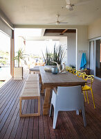 Terrasse mit Esstisch, Holzbank und gelben Stühlen, Deckenventilator und Pflanzendekoration