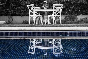 Blick über Pool mit Reflexionen, auf Sitzplatz, weiße Stühle um rundem Tisch mit geschnitztem Fussgestell