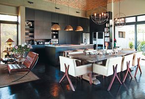 Open-plan kitchen with dark-colored island and cupboards and dining table with modern leather chairs