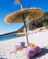 Floor cushions & drinks under straw parasol on sandy beach