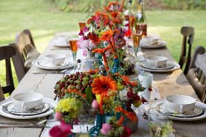 Rustic wooden table set with glasses of aperitifs and vases of autumn flowers