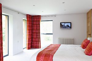 Modern white bedroom with red accents and double bed opposite French windows with floor-length curtains