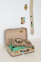 Scatter cushions in open vintage suitcase next to wooden board on wall