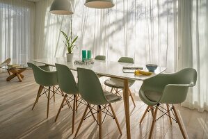 Eleganter Tisch mit grünen Klassikerstühlen vor Fenster mit Gardinen