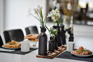 Easter dining table set in white with bottles wrapped in black paper used as vases and black place mats