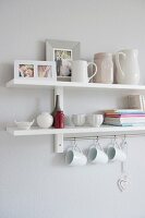 White crockery on a wall shelf with white cups hanging on hooks