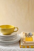 Gestapelte weiße Teller, gelbe Tasse, Tischwäsche und Besteck