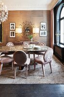Upholstered chairs, oval dining table and framed photos flanking sunburst mirror in elegant dining room