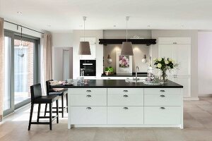 A white kitchen island with a black work surface and black, leather-covered bar stools