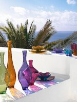 Colourful glass vases and bowls on white wall with view of sea