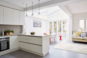 White fitted kitchen, lounge and dining area in modern open-plan interior with terrace view