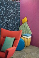 A red armchair and a pile of cushions in front of a two brightly coloured walls