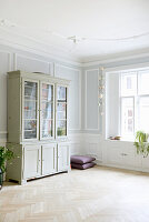 Display cabinet in bright living room with herringbone parquet flooring and wall paneling