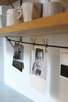 Black and white photos clipped to cord below crockery on shelf with clothes pegs