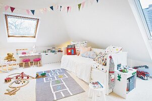 A white bed with colourful cushions and a hopscotch rug in a light and bright young girl's bedroom with slanted roof