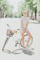 Junge Frau lehnt an Fahrrad in einer Allee